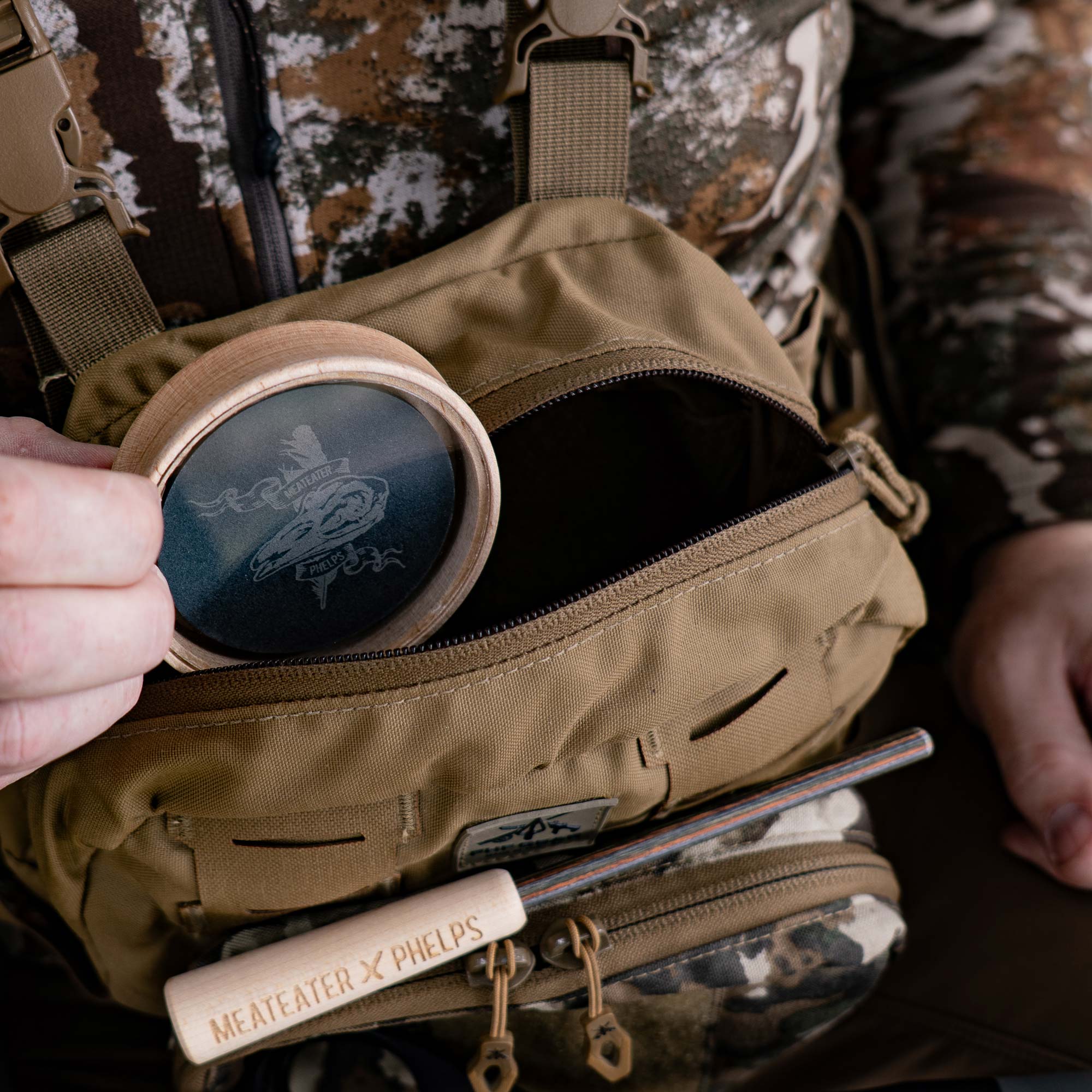 Tan chest rig with Meateater x Phelps game calls: round call & wooden striker.
