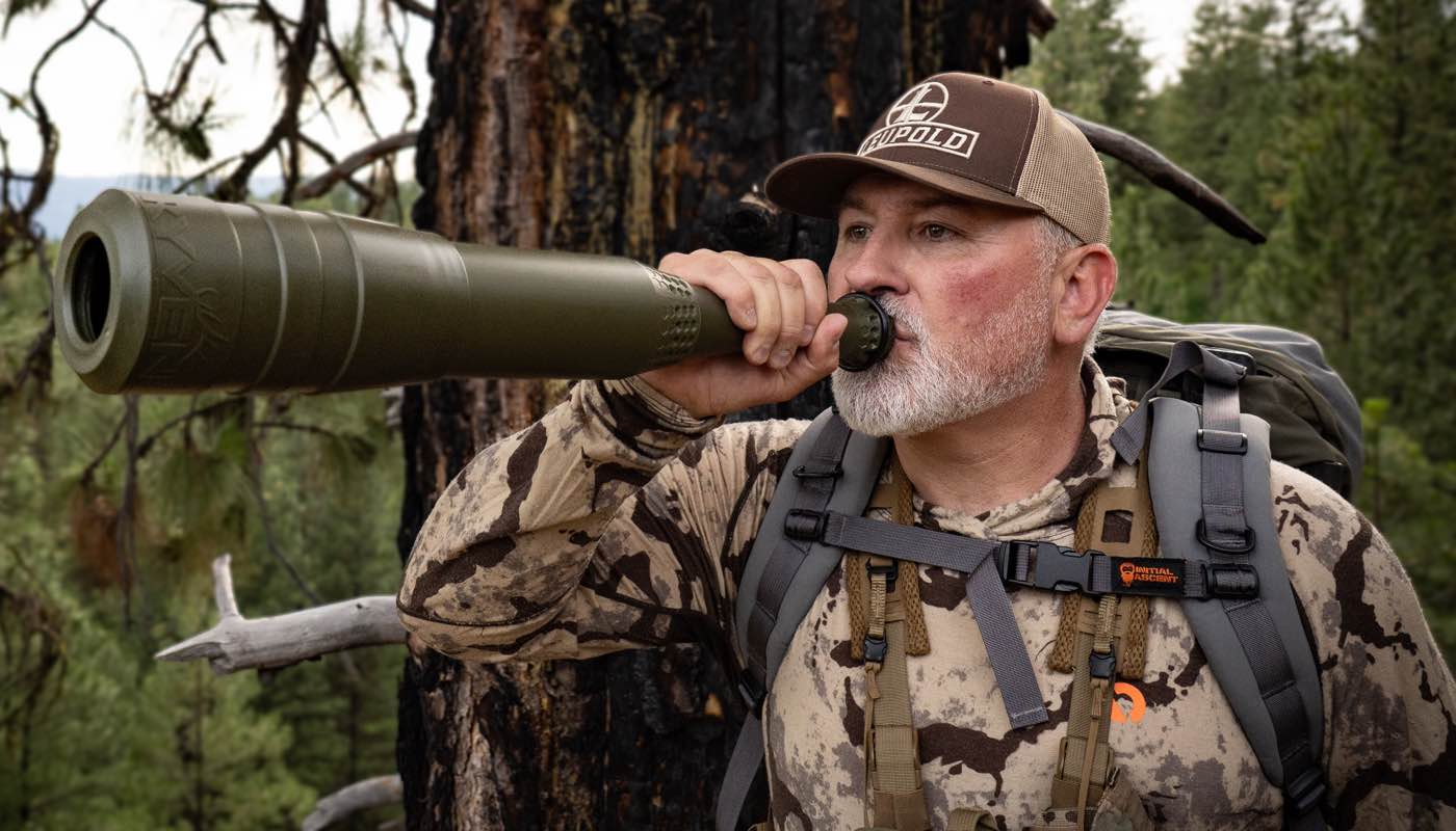 Man blowing olive green elk bugle tube with textured grip.