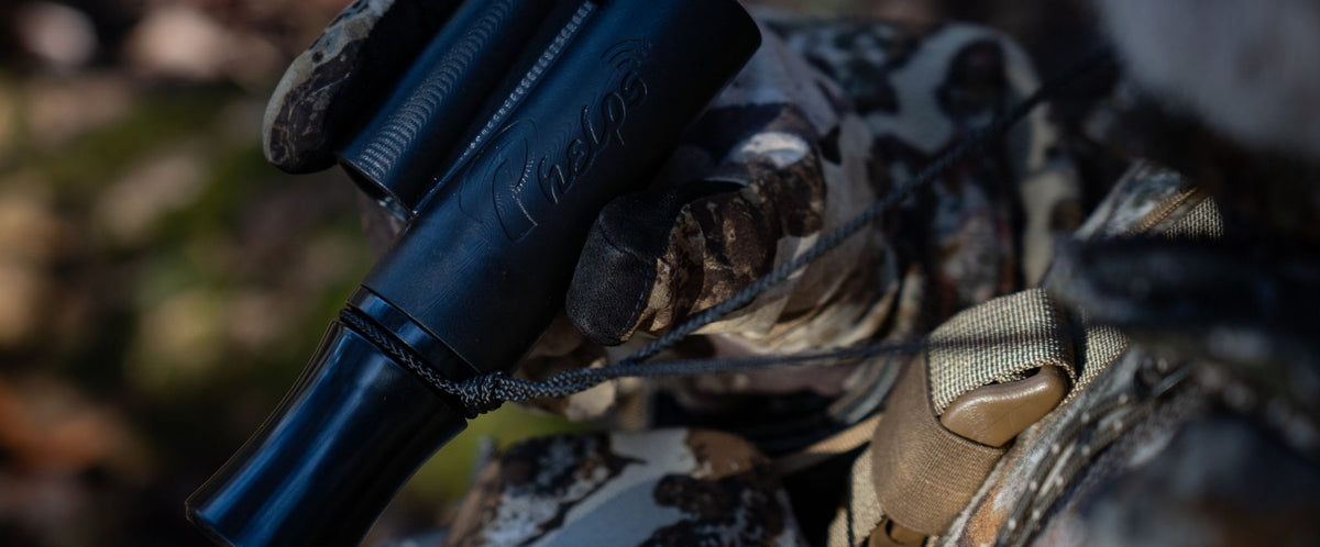 Man in camo suit holding a black Phelps deer call, it has PHELPS branding in it.