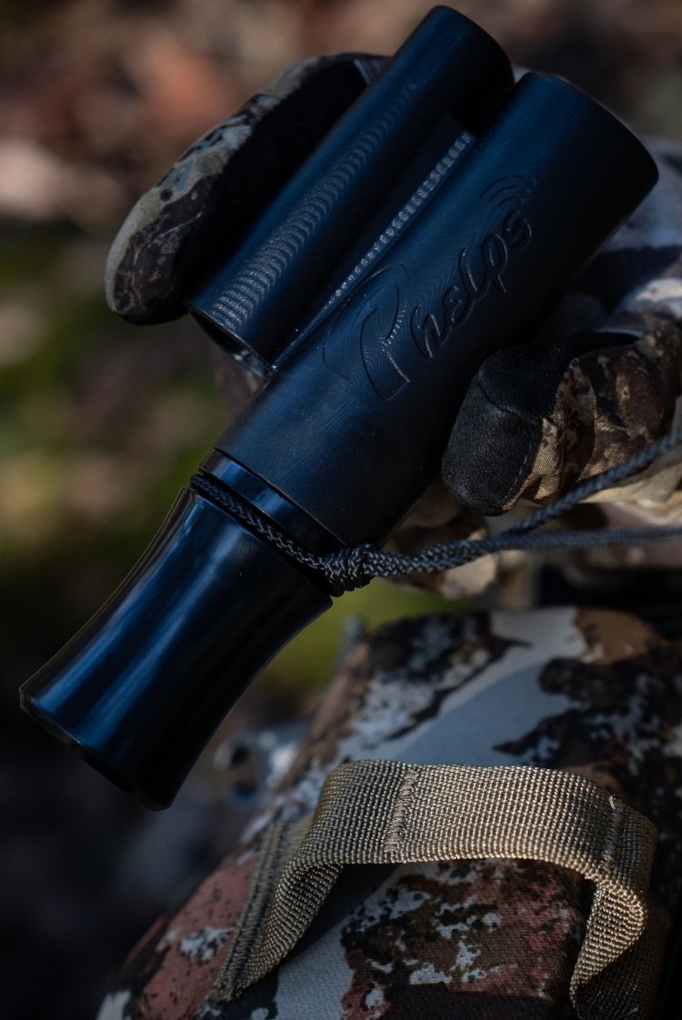 Man in camo suit holding a black Phelps deer call, it has PHELPS branding in it.