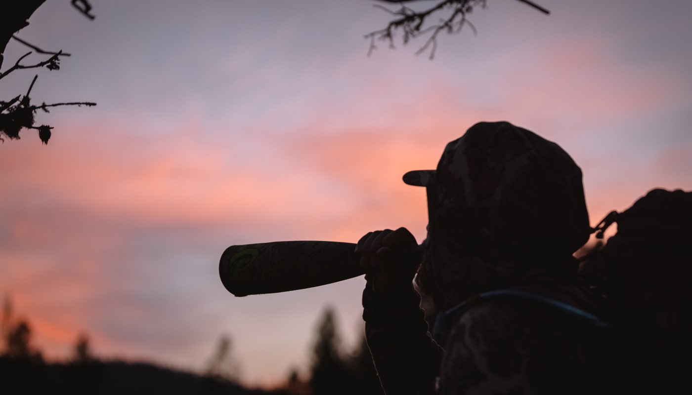 Man using elk bugle tube with sunrise in the background.
